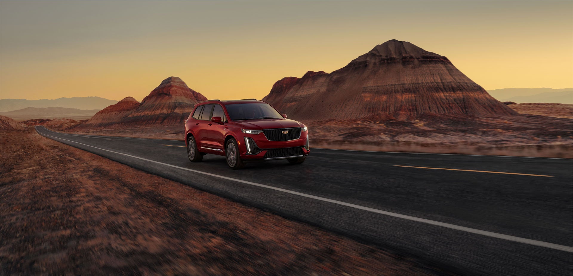 Several Cadillac vehicles parked on a flat surface with the sun rising in the background, casting a warm glow.